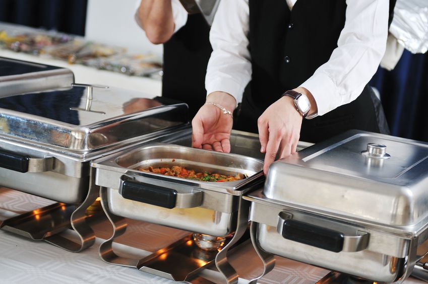 A staff member adjusting a buffet tray at a catered event. 